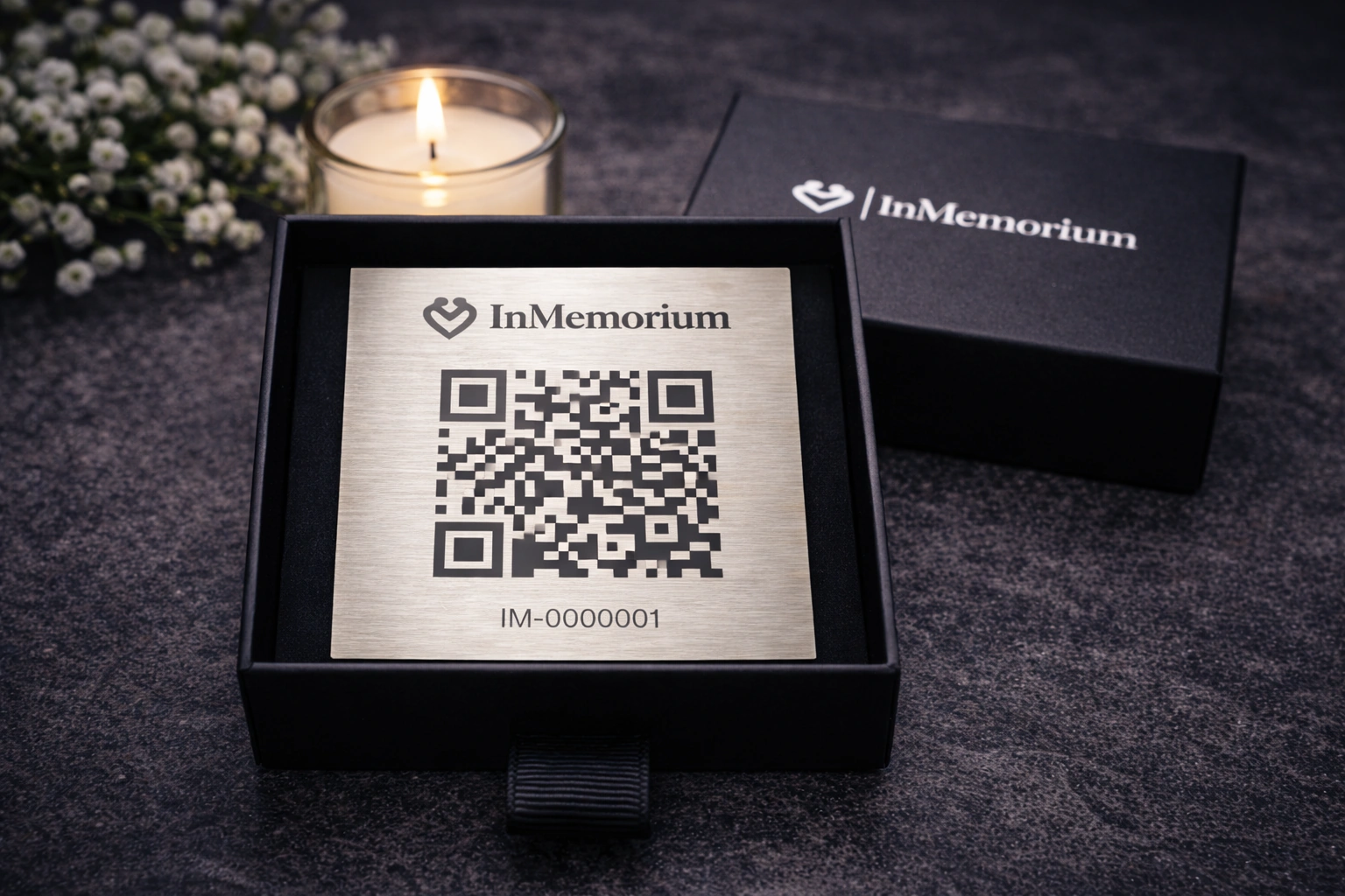 Coffret InMemorium posé sur du granit avec une bougie et des fleurs en arrière-plan.